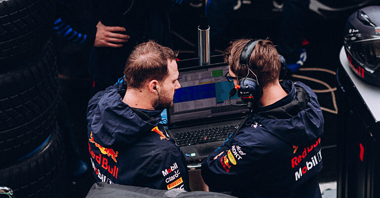 Zwei Mitglieder eines Formel-1-Teams mit Headsets analysieren an einem Laptop Renndaten in der Box.