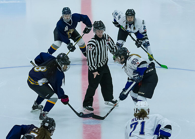 Bully im Eishockey: Ein Schiedsrichter lässt den Puck zwischen zwei Spielerinnen konkurrierender Teams fallen.