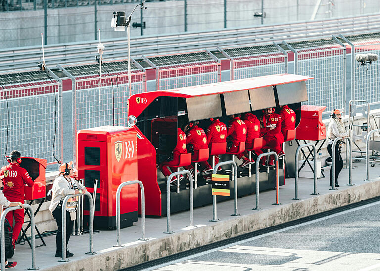 Mitglieder des Ferrari-Formel-1-Teams sitzen am roten Kommandostand in der Boxengasse einer Rennstrecke.
